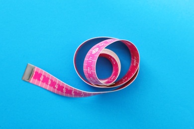 Pink measuring tape on light blue background, top view
