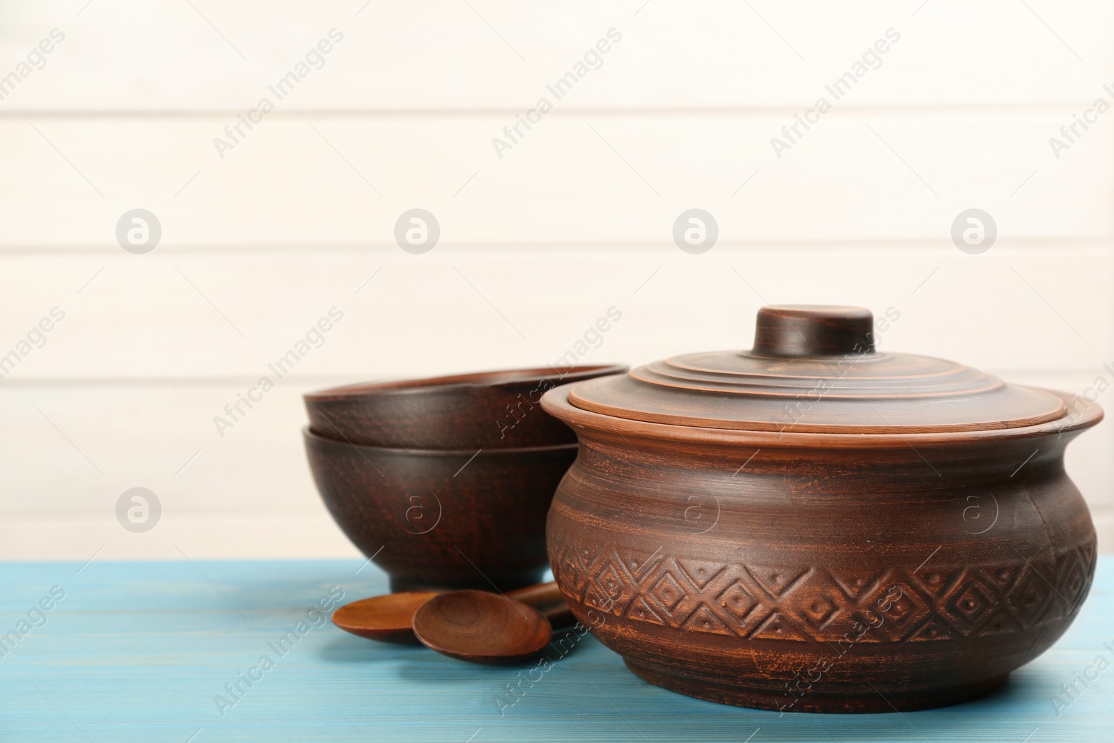 Photo of Set of clay utensils on light blue wooden table. Space for text