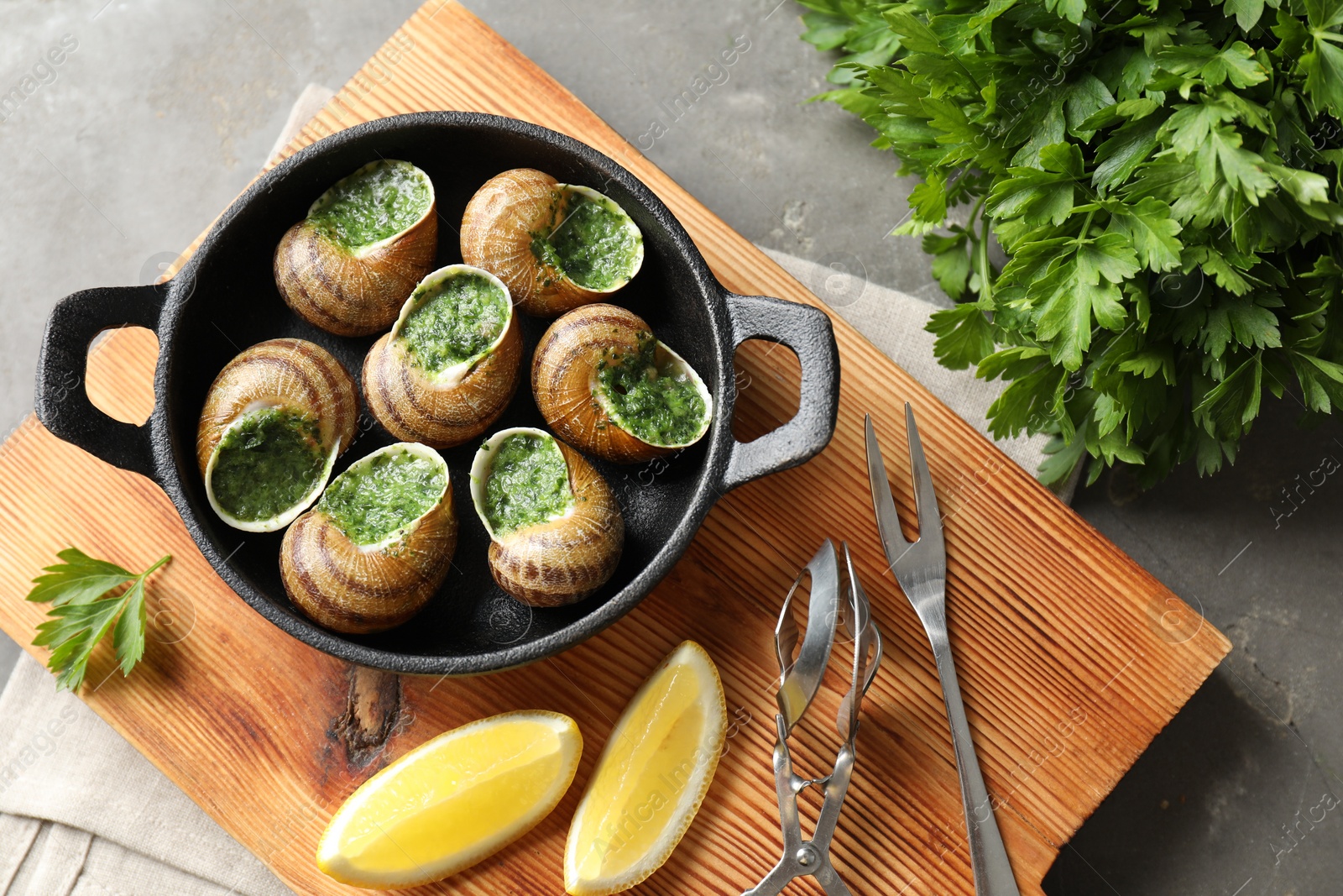 Photo of Delicious cooked snails in baking dish served on grey textured table, flat lay