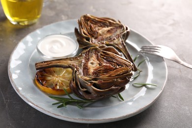 Photo of Plate with tasty grilled artichoke served on grey table, closeup