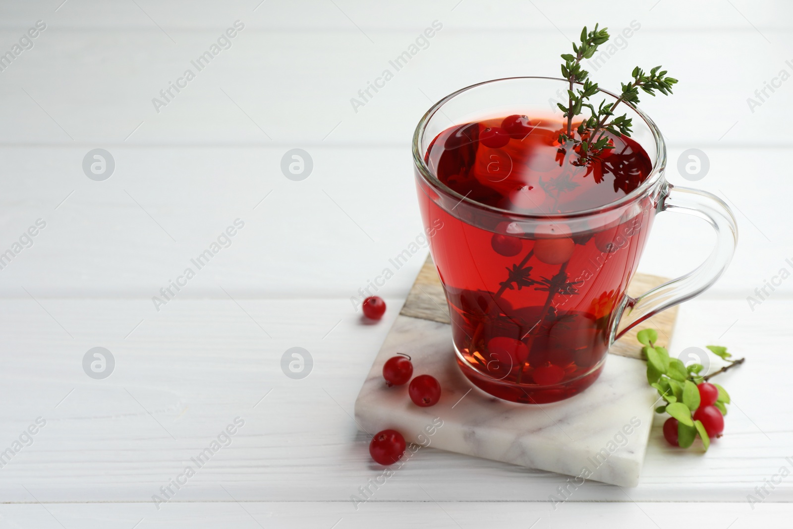 Photo of Tasty hot cranberry tea with thyme and fresh berries in glass cup on white wooden table