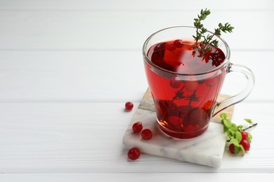 Tasty hot cranberry tea with thyme and fresh berries in glass cup on white wooden table