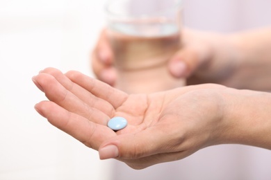 Woman holding pill and glass of water on blurred background, closeup. Space for text