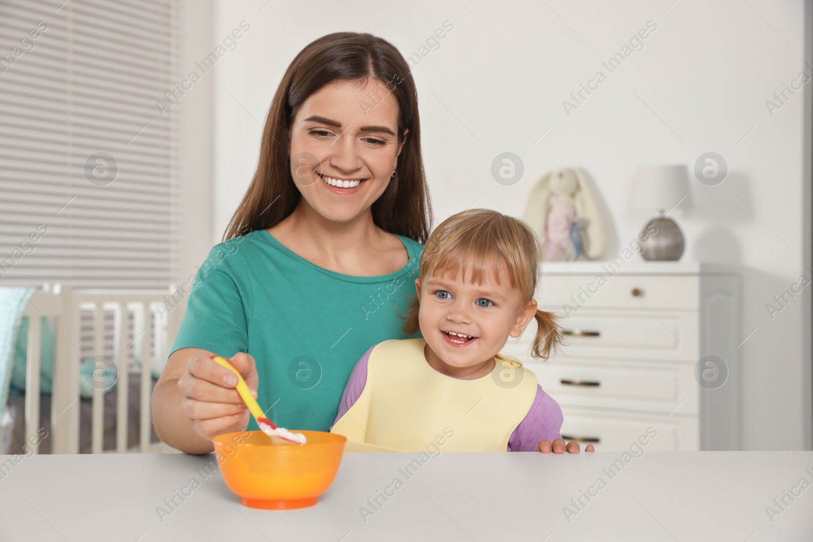 Photo of Mother feeding her cute little child with yogurt at white table in room