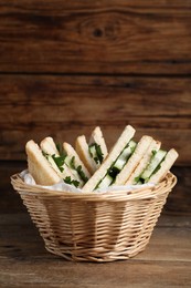 Photo of Tasty sandwiches with cucumber and parsley in wicker basket on wooden table