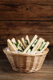 Tasty sandwiches with cucumber and parsley in wicker basket on wooden table