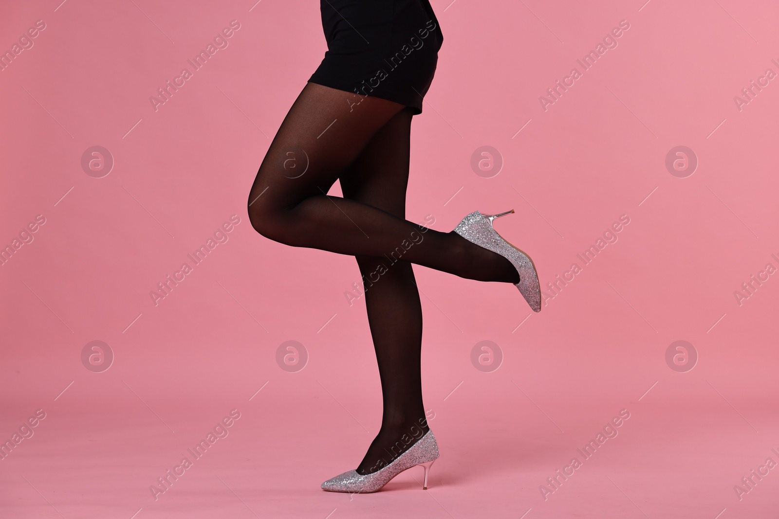 Photo of Woman with beautiful long legs wearing black tights and stylish shoes on pink background, closeup