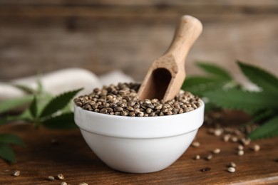 Photo of Bowl with hemp seeds and scoop on wooden board, closeup