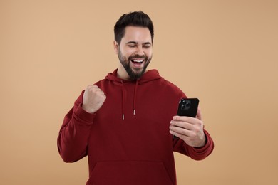 Happy young man using smartphone on beige background