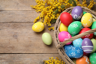 Photo of Colorful Easter eggs and mimosa flowers on wooden background, flat lay. Space for text