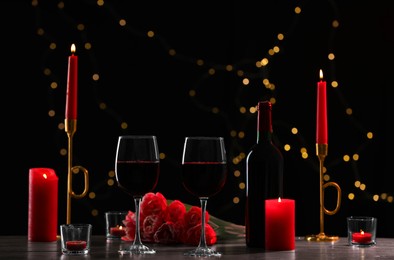 Glasses of red wine, tulip flowers and burning candles on black background against blurred lights. Romantic atmosphere