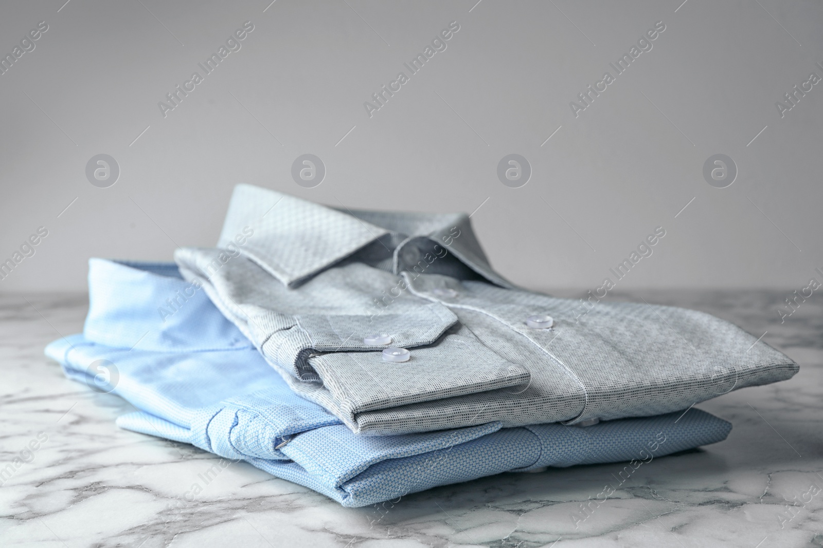 Photo of Classic shirts on marble table against light background