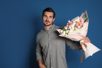 Young handsome man with beautiful flower bouquet on blue background