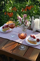 Vase with spring flowers, wine and cake on table served for romantic date in garden