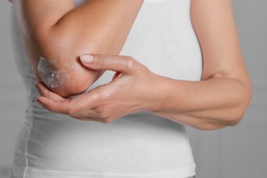 Photo of Woman applying body cream on elbow indoors, closeup