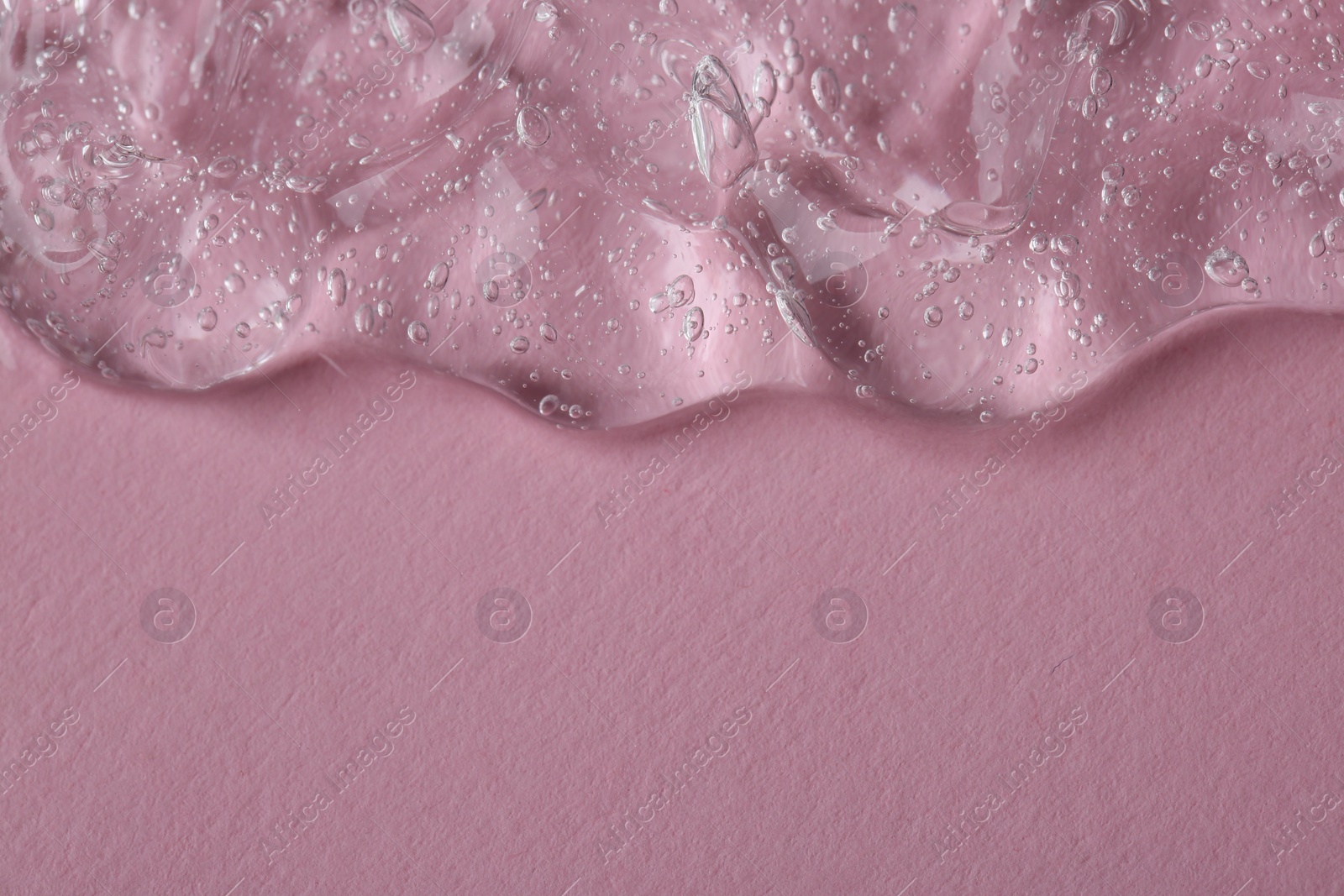 Photo of Clear cosmetic serum on pink background, macro view. Space for text
