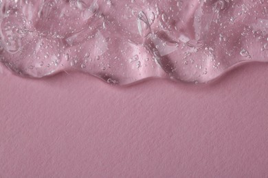 Clear cosmetic serum on pink background, macro view. Space for text