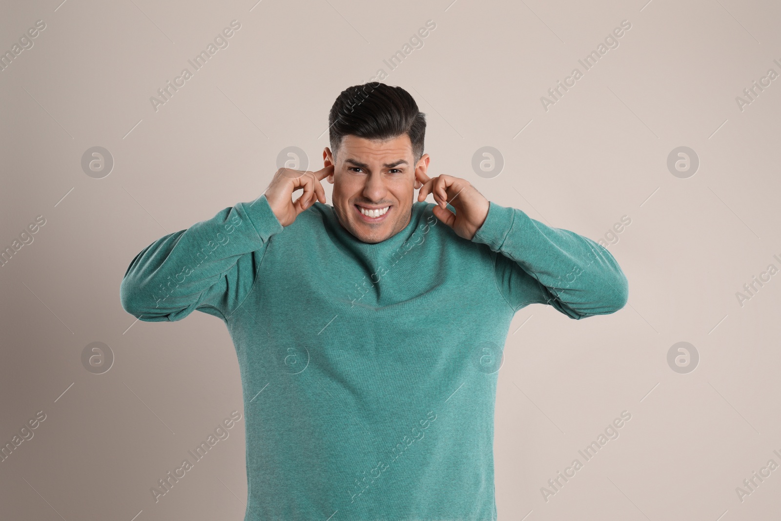 Photo of Emotional man covering ears with fingers on beige background