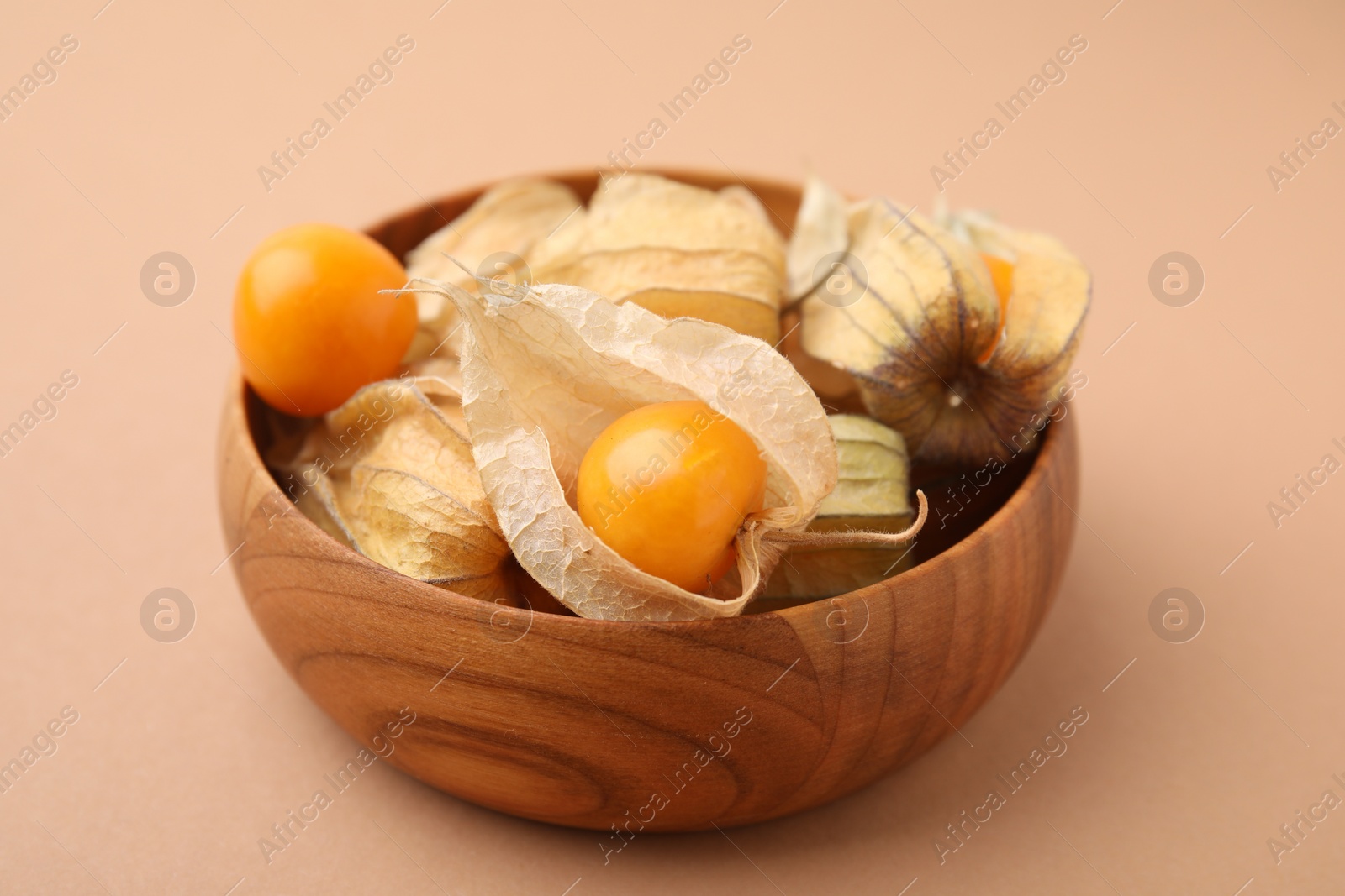 Photo of Ripe physalis fruits with calyxes in bowl on beige background, closeup