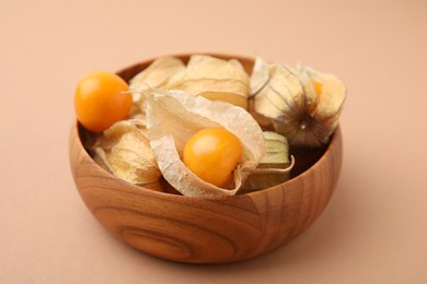 Ripe physalis fruits with calyxes in bowl on beige background, closeup