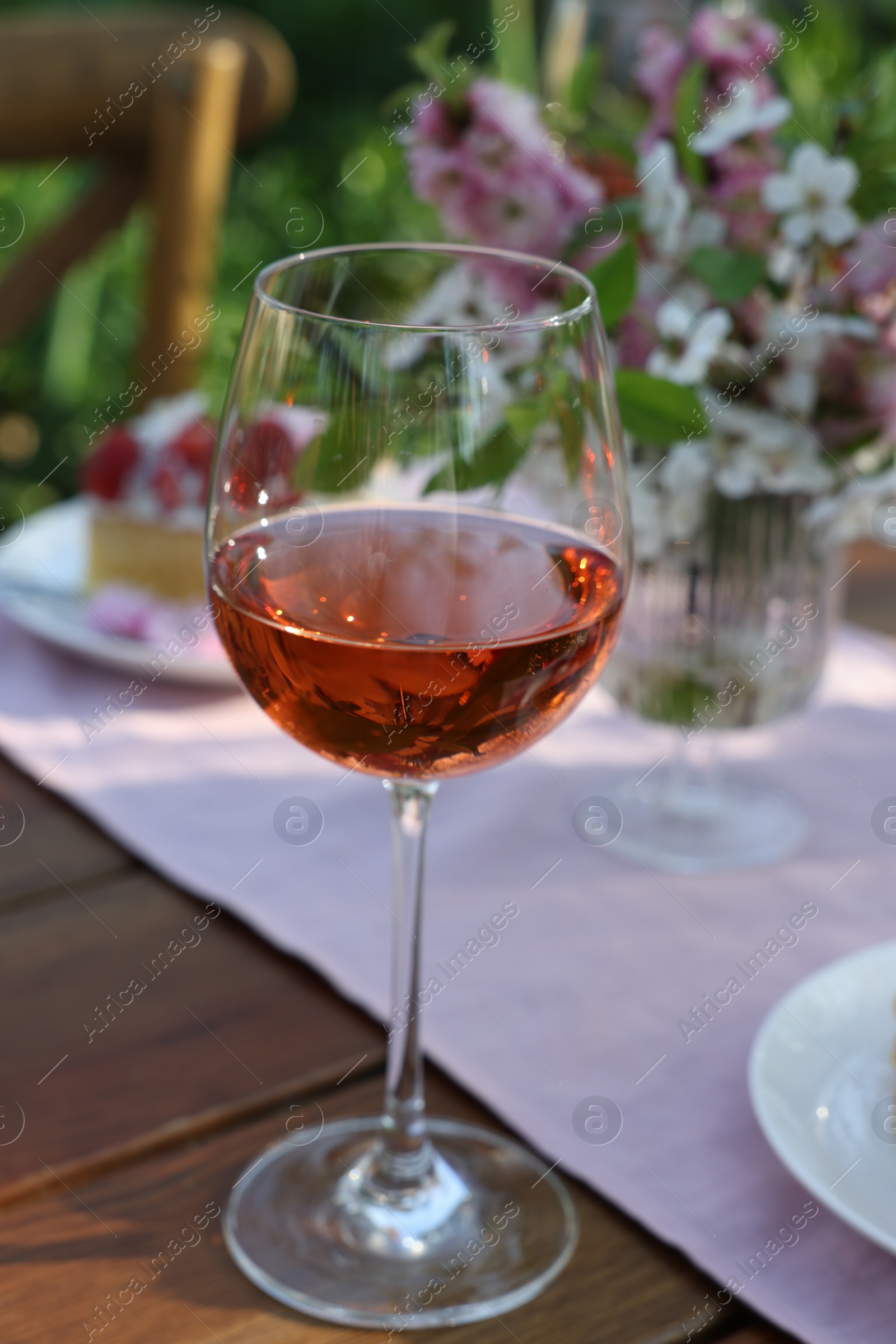 Photo of Glass of rose wine on table served for romantic date in garden