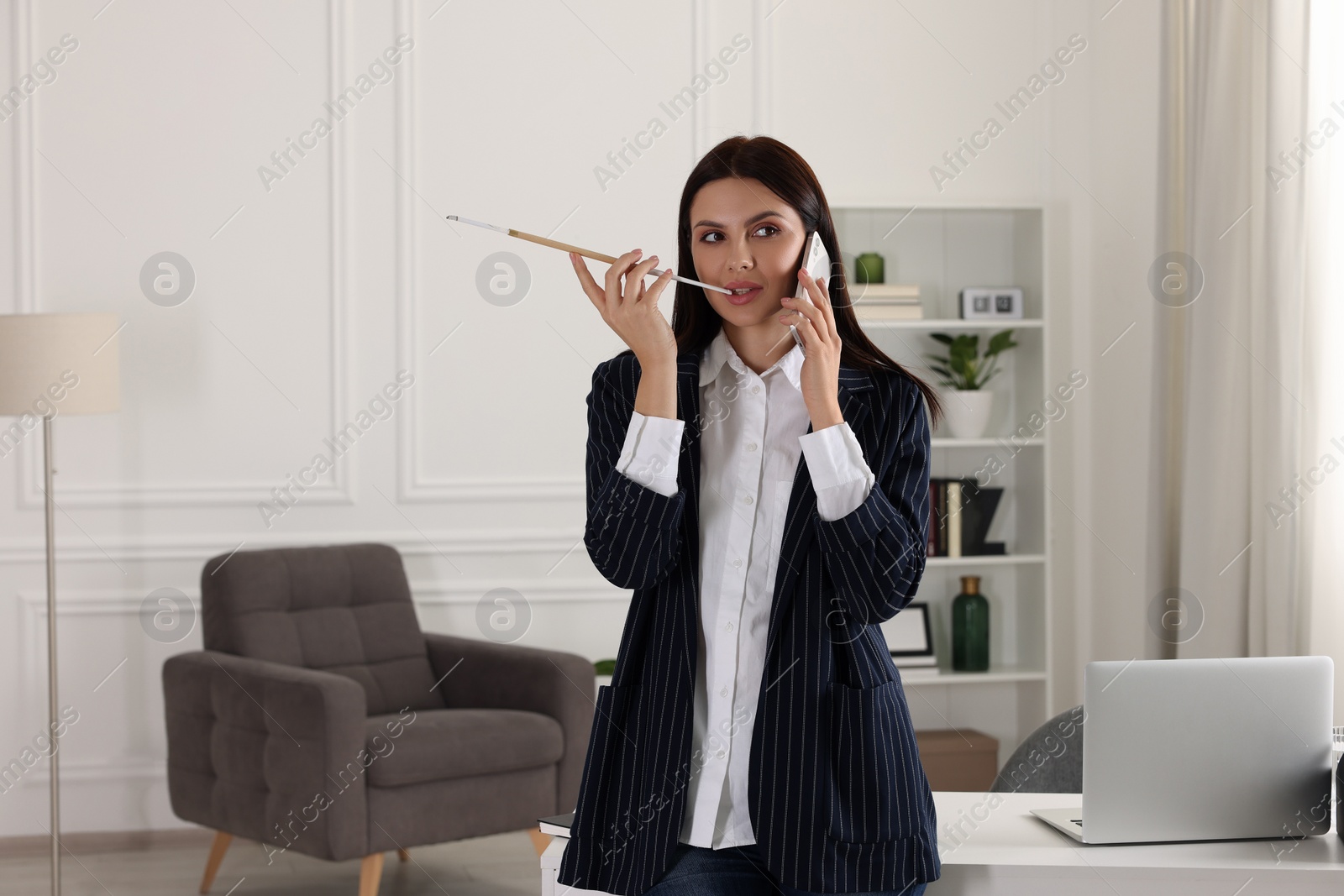 Photo of Woman using long cigarette holder for smoking and talking on phone in office