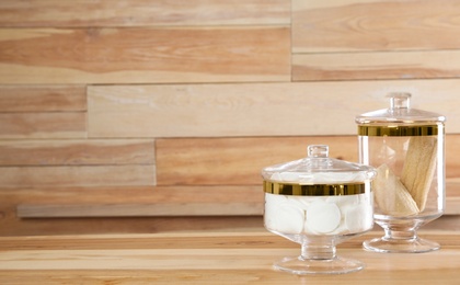 Decorative glass jars with cotton pads and loofahs on table against wooden background. Space for text