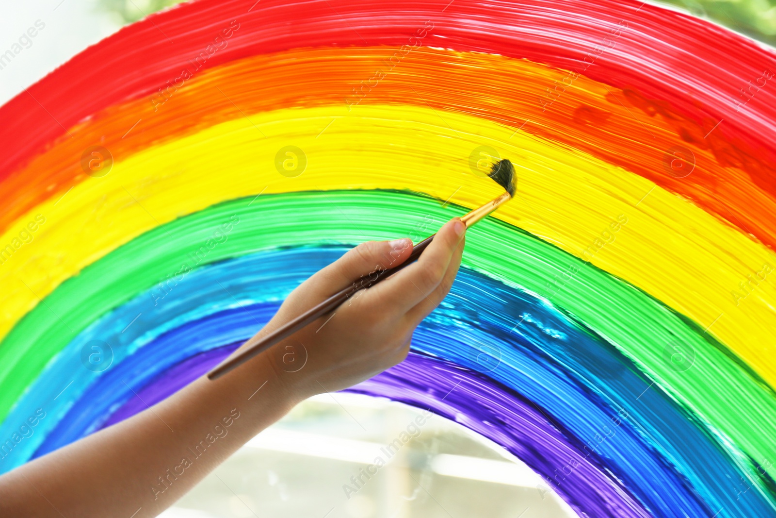 Photo of Little child drawing rainbow on window, closeup. Stay at home concept