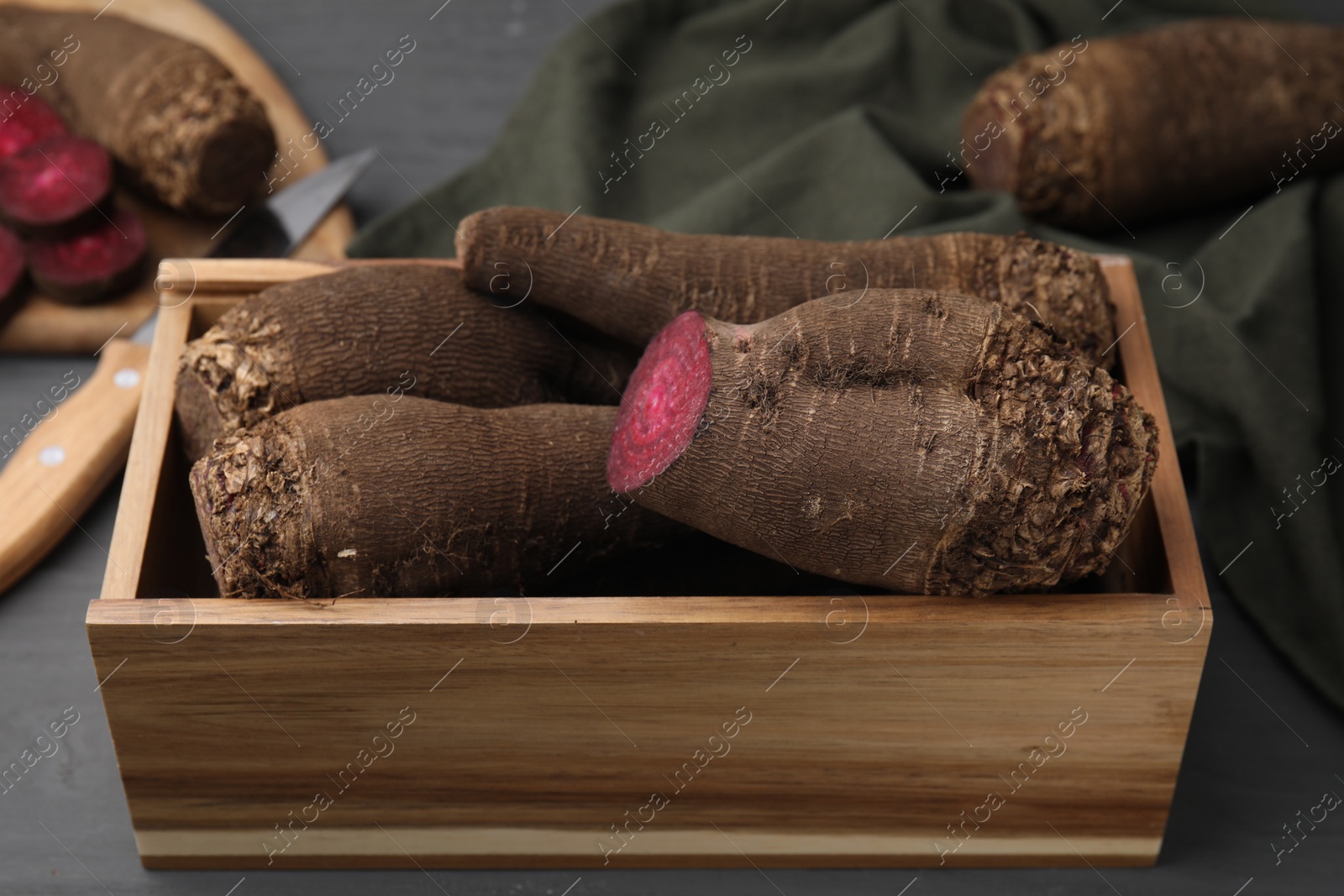 Photo of Whole and cut red beets in wooden crate on table, closeup