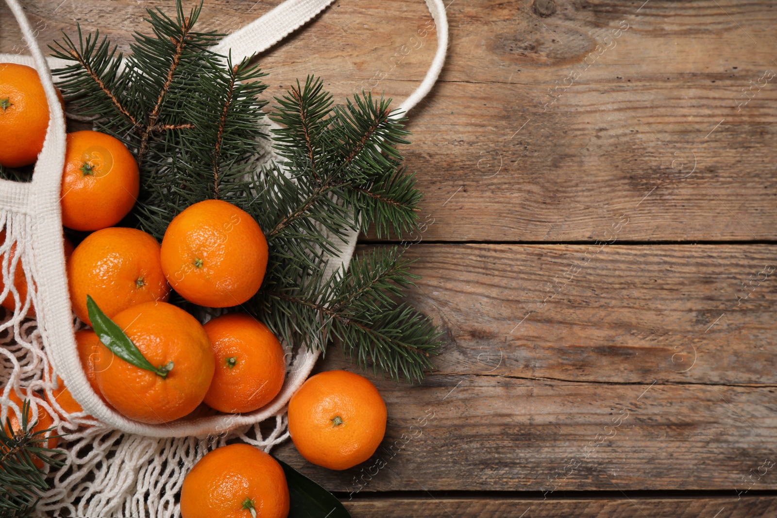 Photo of Fresh ripe tangerines, fir tree branches and mesh bag on wooden table, flat lay. Space for text