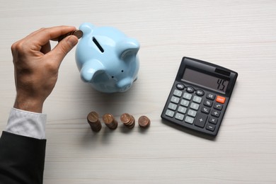 Photo of Budget planning. Businessman putting coin into piggy bank at light wooden table, top view