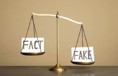 Photo of Scales with words FACT and FAKE on wooden table