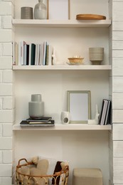 Books, empty frames and different decor on shelves indoors. Interior design