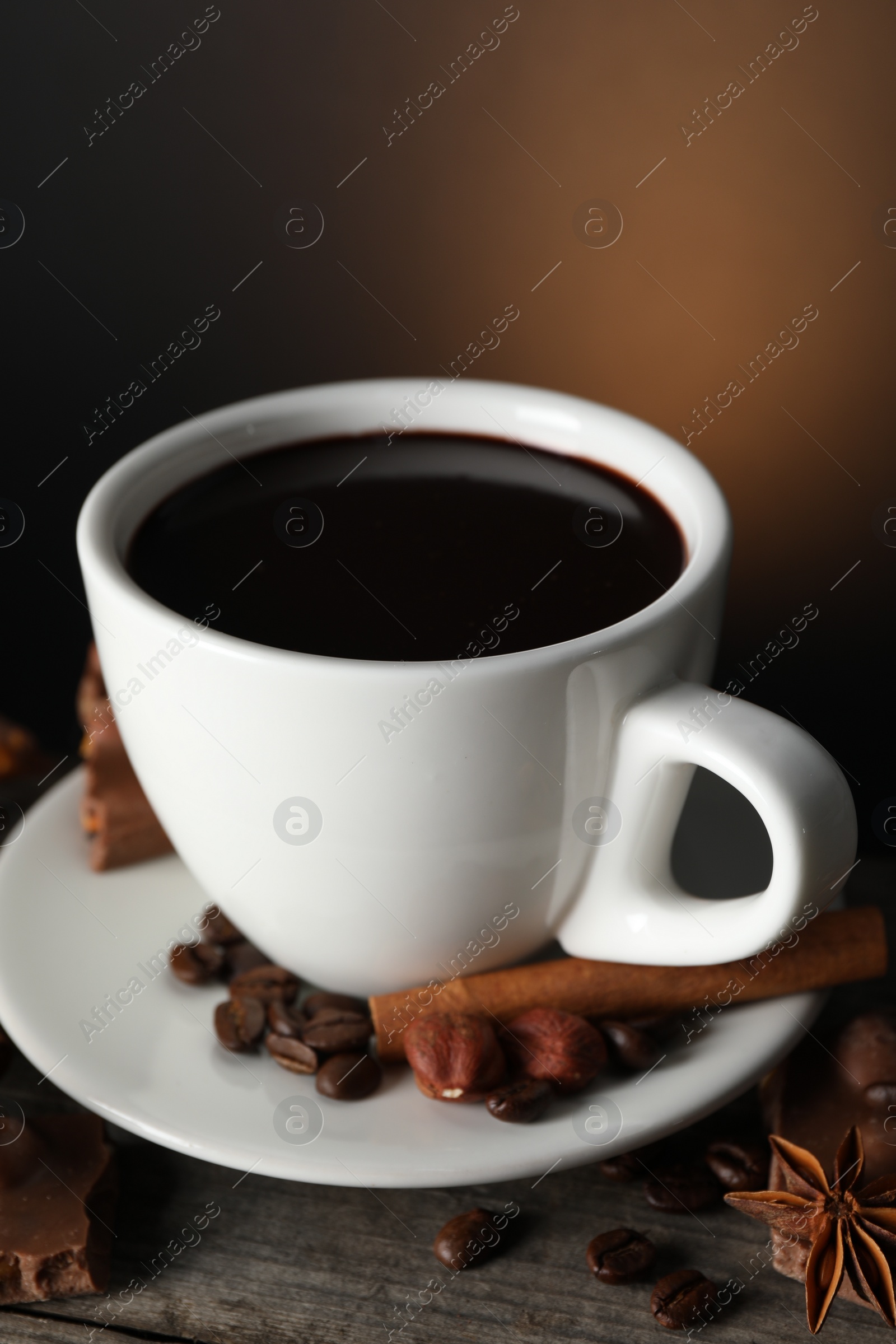 Photo of Cup of delicious hot chocolate, spices and coffee beans on wooden table