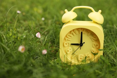 Yellow alarm clock on green grass outdoors, closeup