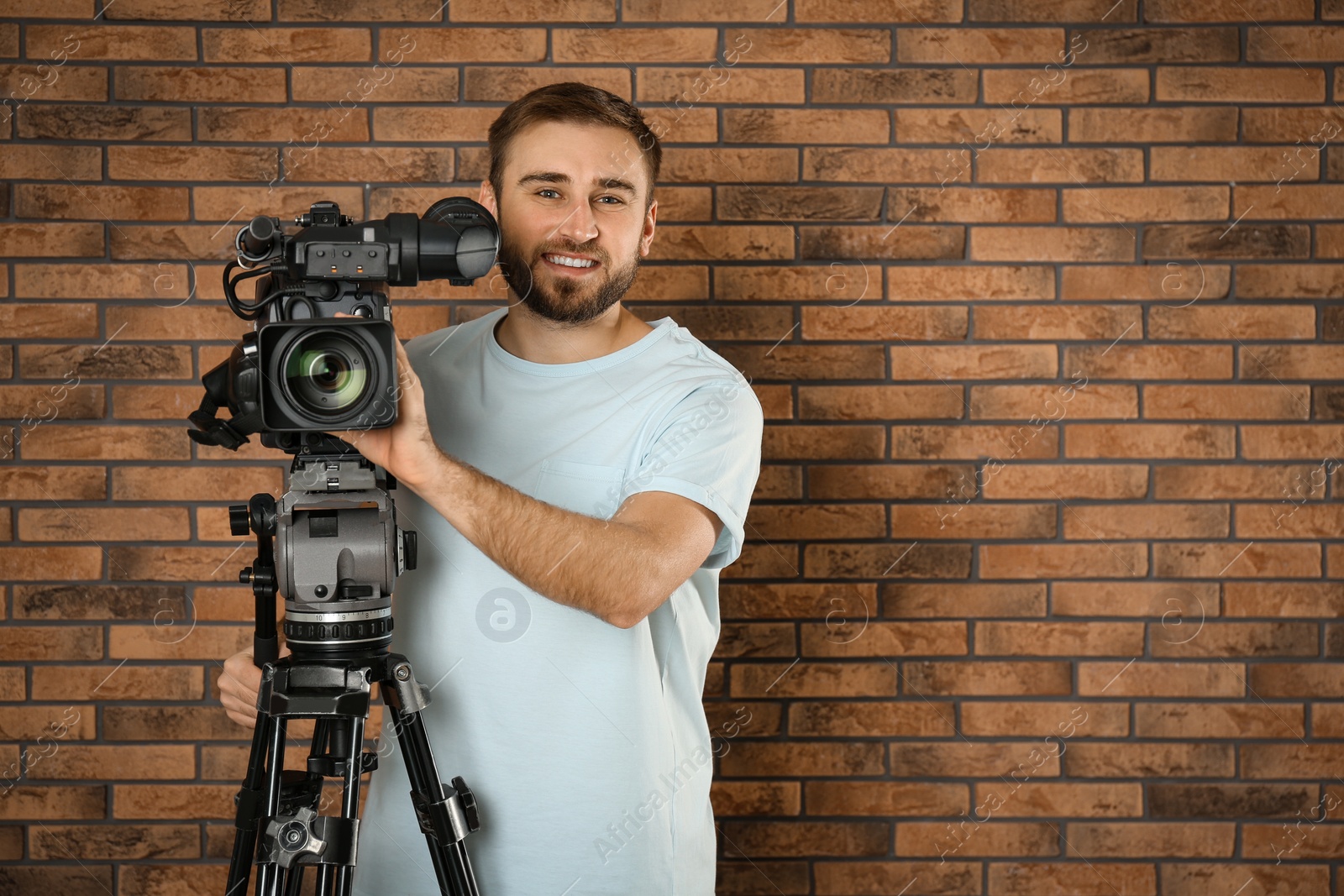 Photo of Operator with professional video camera near brick wall, space for text