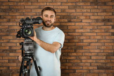Operator with professional video camera near brick wall, space for text