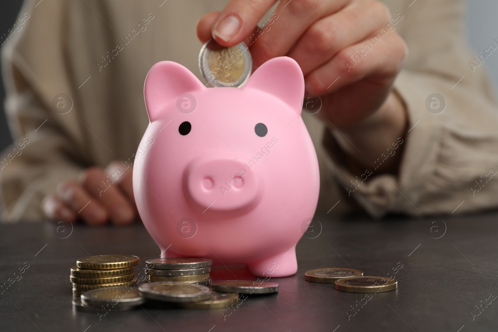 Photo of Woman putting coin into pink piggy bank at black table, closeup