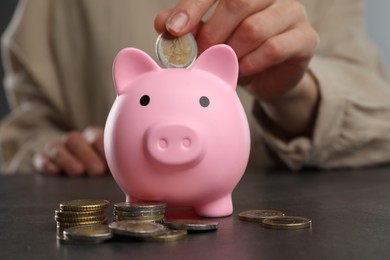 Woman putting coin into pink piggy bank at black table, closeup