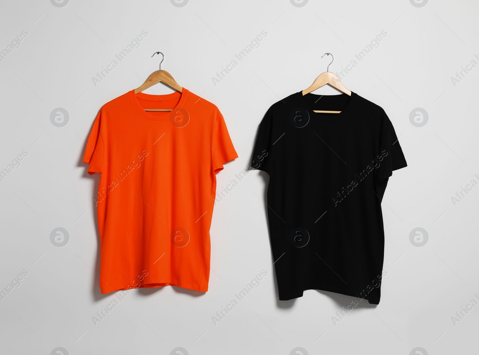 Photo of Hangers with different t-shirts on light wall. Mockup for design