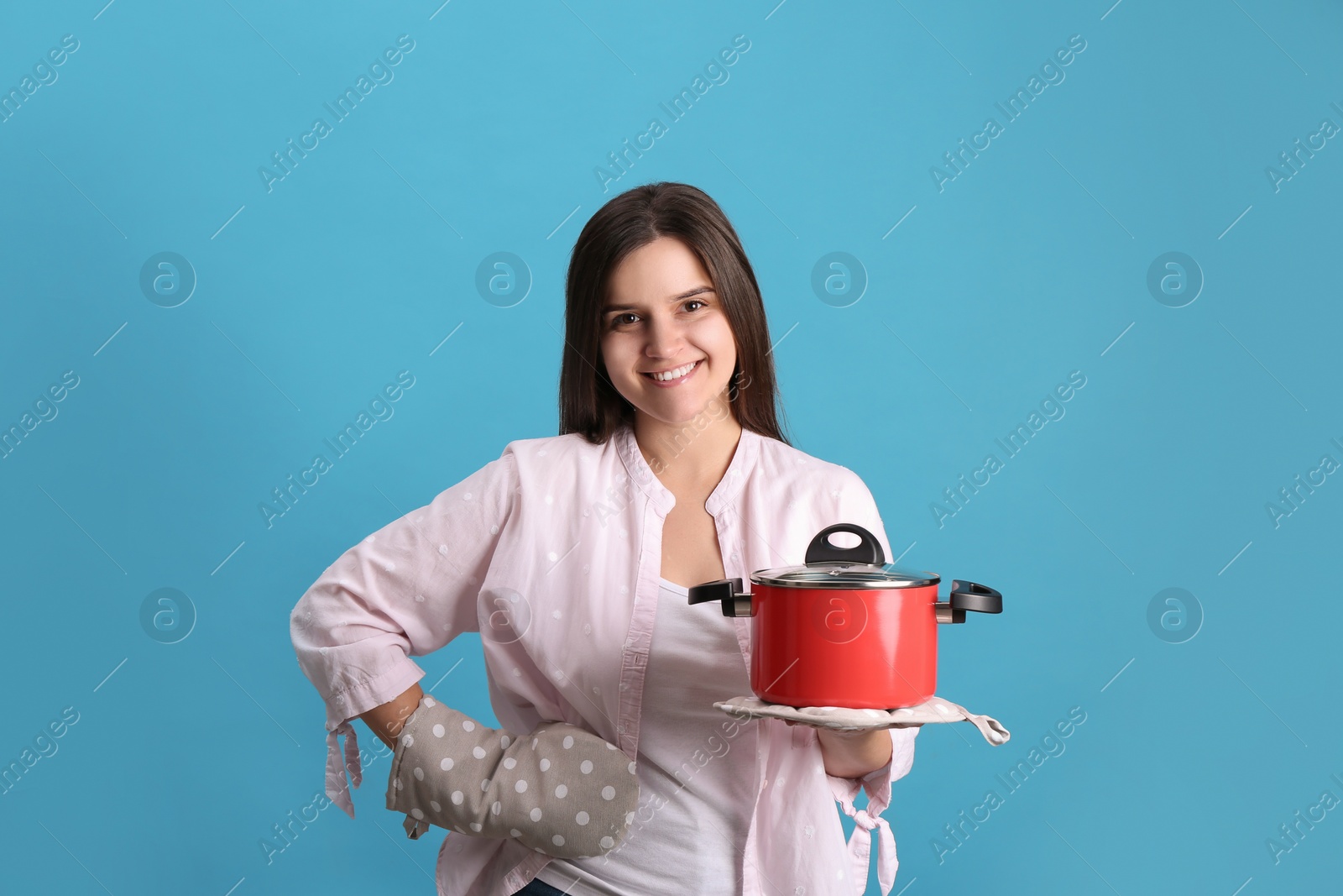 Photo of Happy young woman with cooking pot on light blue background