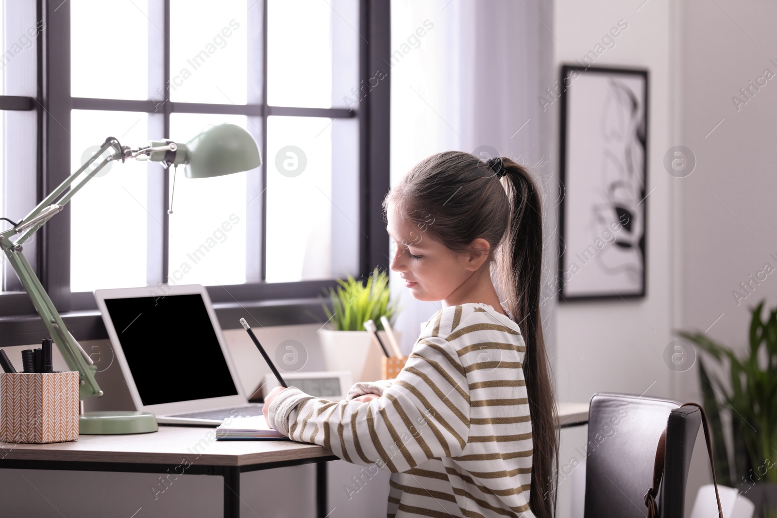 Photo of Pretty preteen girl doing homework at table in room