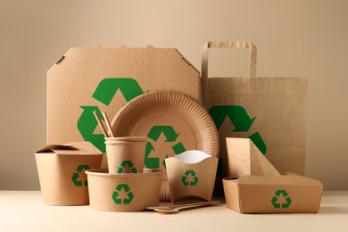 Set of eco friendly food packaging with recycling symbols on table against beige background