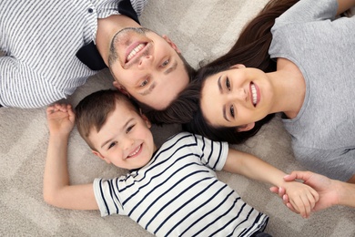 Photo of Happy parents and their son lying together on floor, view from above. Family time