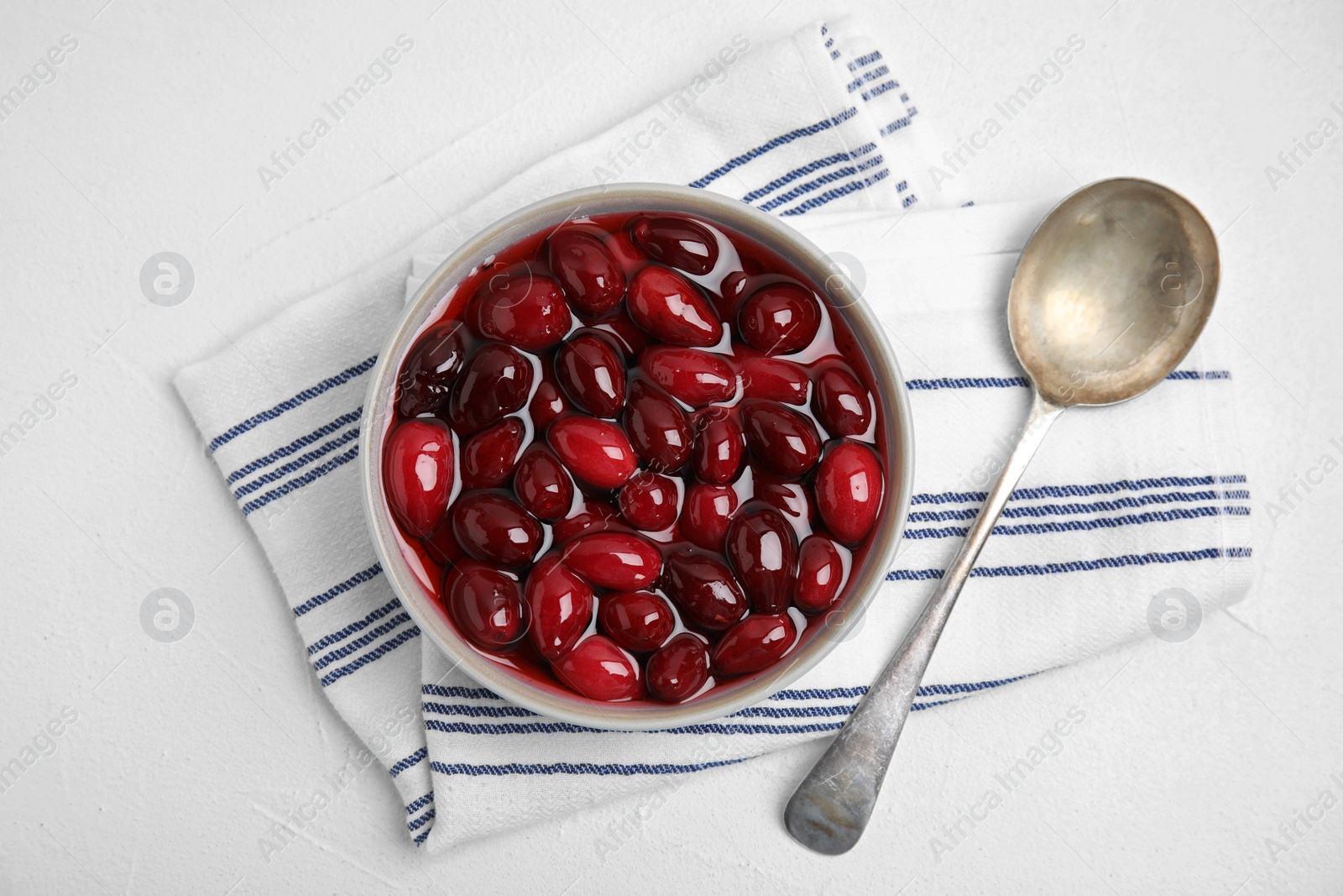 Photo of Delicious dogwood jam with berries in bowl and spoon on white table, flat lay