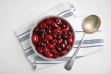 Photo of Delicious dogwood jam with berries in bowl and spoon on white table, flat lay