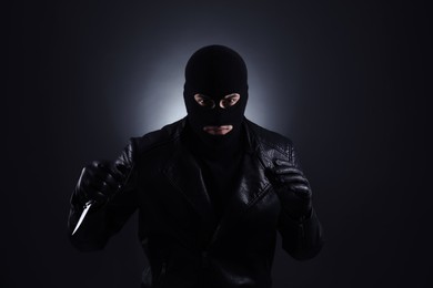 Man wearing knitted balaclava with knife on black background