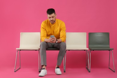 Man with smartphone waiting for job interview on pink background