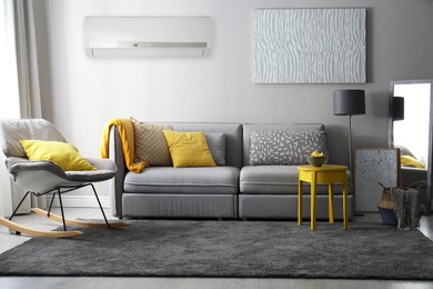Image of Modern air conditioner on light grey wall in living room with stylish furniture