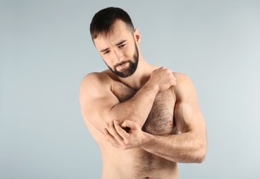 Young man suffering from pain in elbow on light background